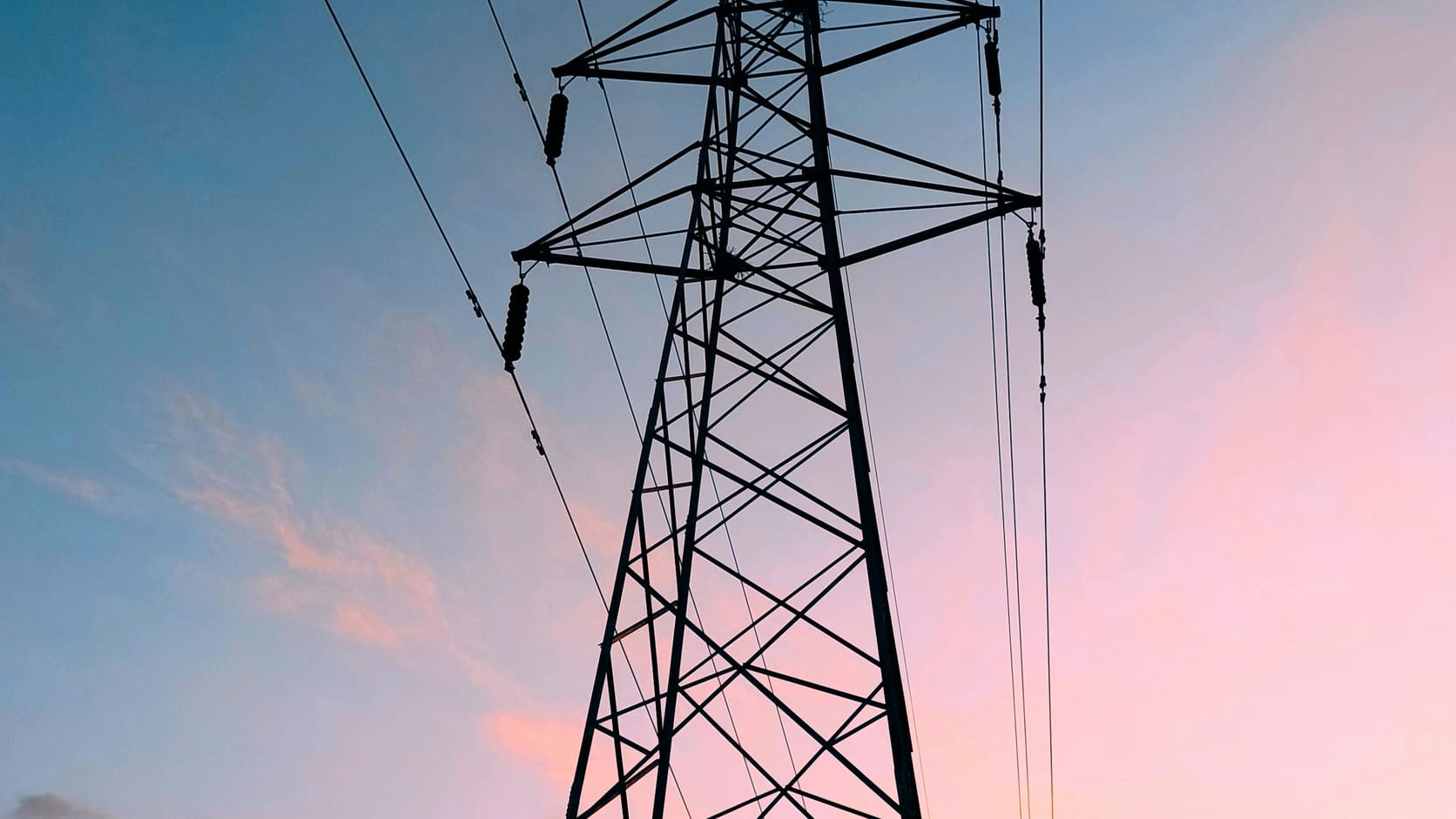 Illustrative electricity transmission tower silhouetted against a dusk sky