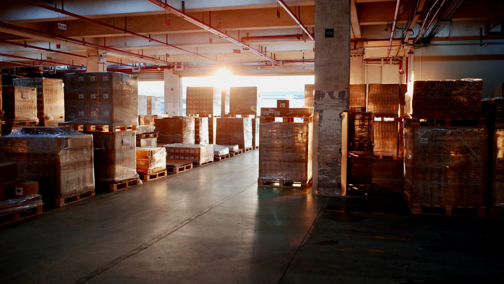 Illustrative warehouse aisle with wrapped pallets of goods and warm evening light